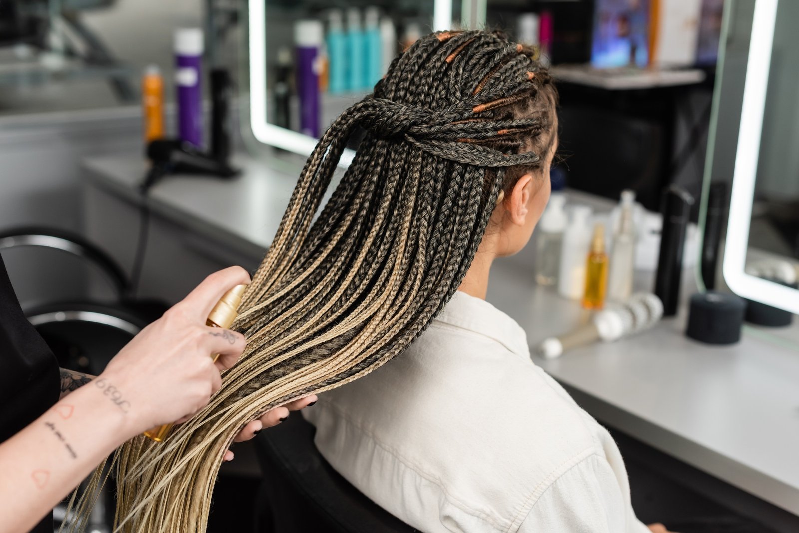 hair salon, tattooed hairdresser applying hair product on braids of woman in salon, spray bottle,