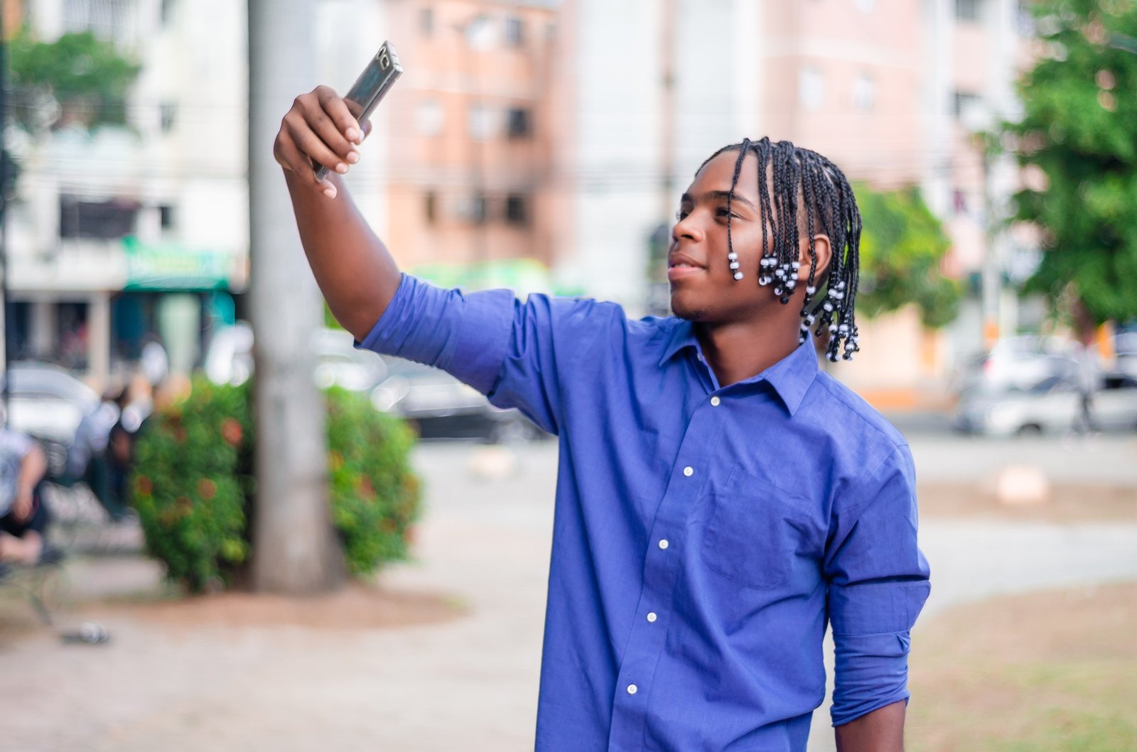 young latino dominican man with dark skin and curly and braided hair in the city, taking a selfie